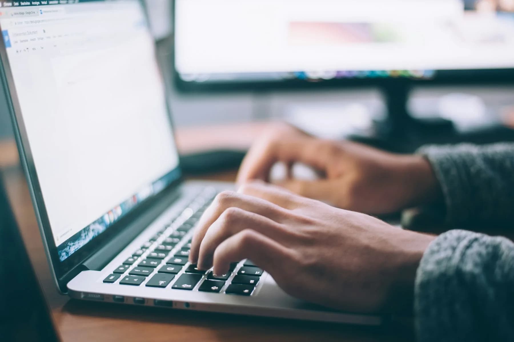 Hands typing on a laptop beside a notebook
